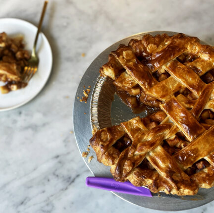 Photo of a apple pie with a slice cut out and placed on a nearby plate