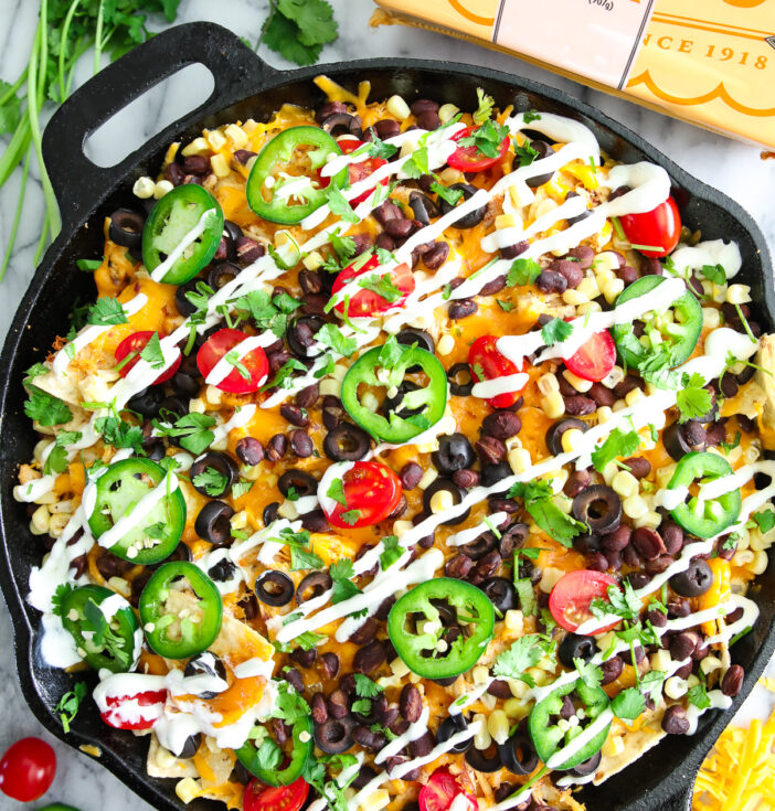 A cast iron pan filled with nachos and other colorful ingredients
