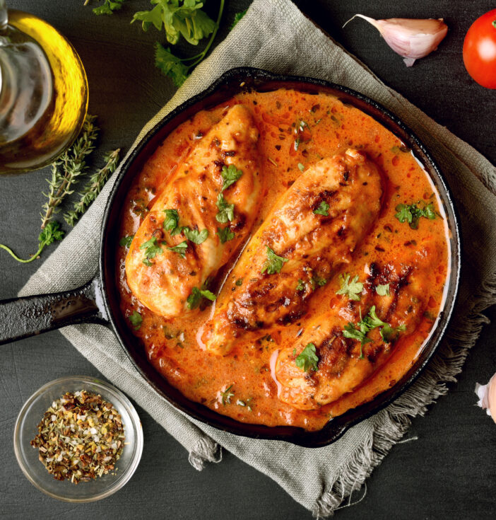A cast iron pot with three chicken breasts in orange sauce