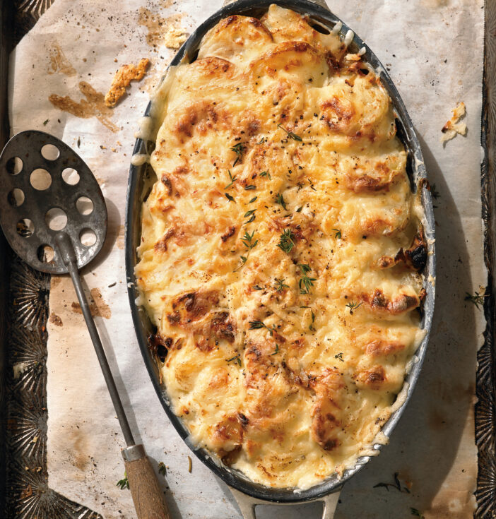 A pan full of cooked au gratin potatoes and a spoon with holes in it