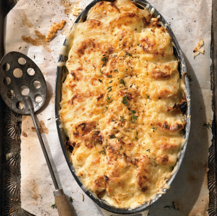 A pan full of cooked au gratin potatoes and a spoon with holes in it