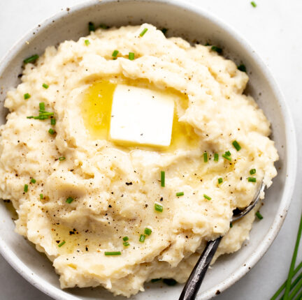 A bowl of mashed potatoes and cauliflower with butter and chives