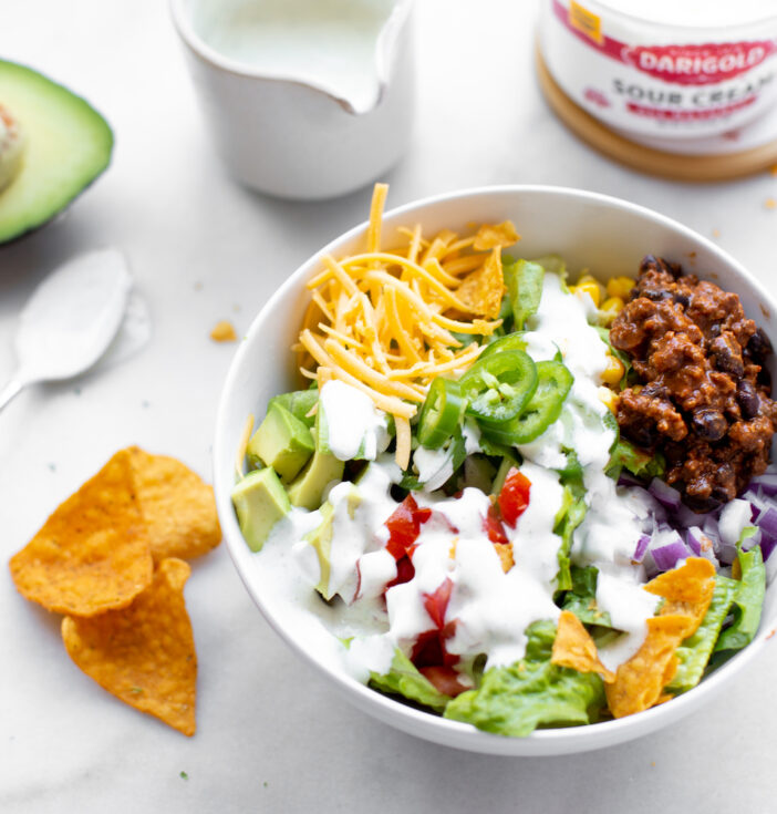 A bowl of taco salad, with chips, an avocado and sour cream