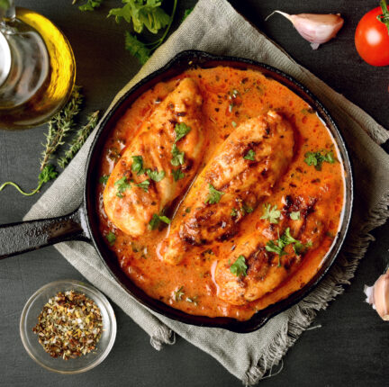 A cast iron pot with three chicken breasts in orange sauce