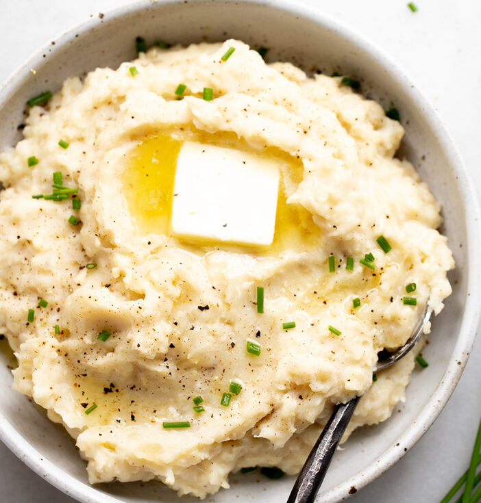 A bowl of mashed potatoes and cauliflower with butter and chives