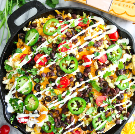 A cast iron pan filled with nachos and other colorful ingredients